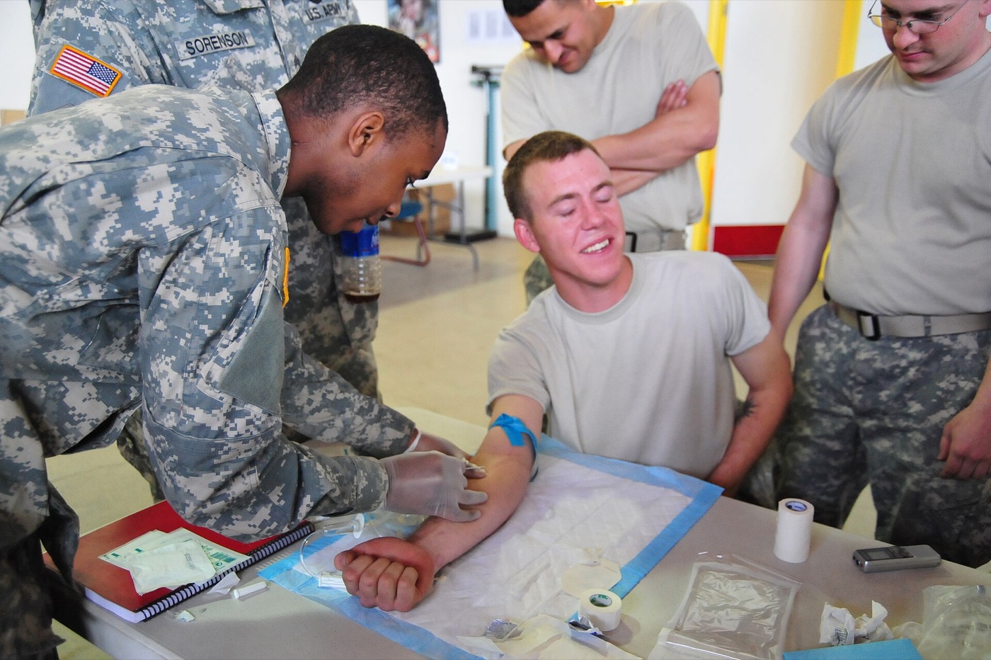 A U.S. Army soldier practising inserting an IV line into another soldier's arm while others watch